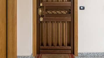 A wooden door with a vertical panel design, a doormat, and a wall-mounted device.