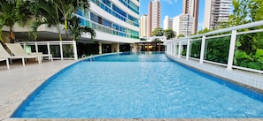 A swimming pool with lounge chairs, surrounded by tall buildings and greenery. - COBAR0150 - Edificio Top House (Salvador)