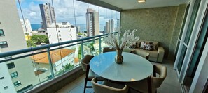 A balcony with a round table and chairs, a vase with white flowers, and a sofa with patterned cushions. - COBAR0150 - Edificio Top House (Salvador)