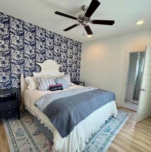 A bedroom with a patterned wallpaper, a ceiling fan, a bed with a white headboard, and a nightstand. - Join us at the Southern Plain Cottage 3-bedroom house close to Auburn campus (Auburn)