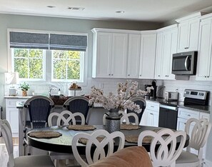 A kitchen with white cabinets, a dining table with chairs, a vase with flowers, and a microwave. - Join us at the Southern Plain Cottage 3-bedroom house close to Auburn campus (Auburn)