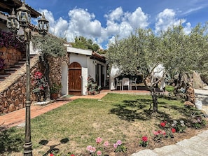 Ein Haus mit Steinstufen, heller Fassade und einem kleinen Garten mit Blumen und einem Baum.
