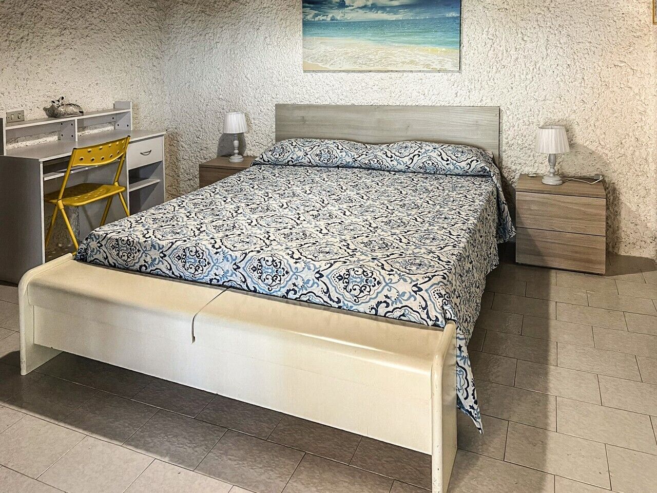 Un dormitorio con cama, escritorio, silla, mesita de noche y lámpara.