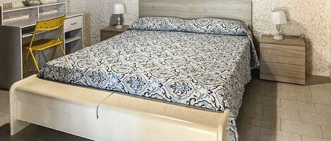 Un dormitorio con cama, escritorio, silla, mesita de noche y lámpara.
