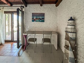 Ein Zimmer mit Tisch und Stühlen, einem Bild an der Wand, einem Holzregal und einer Tür, die nach draußen führt.