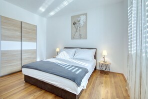 Ein modernes Schlafzimmer mit einem großen Bett, zwei Nachttischen mit Lampen, einem Holzboden und einem Gemälde an der Wand.
