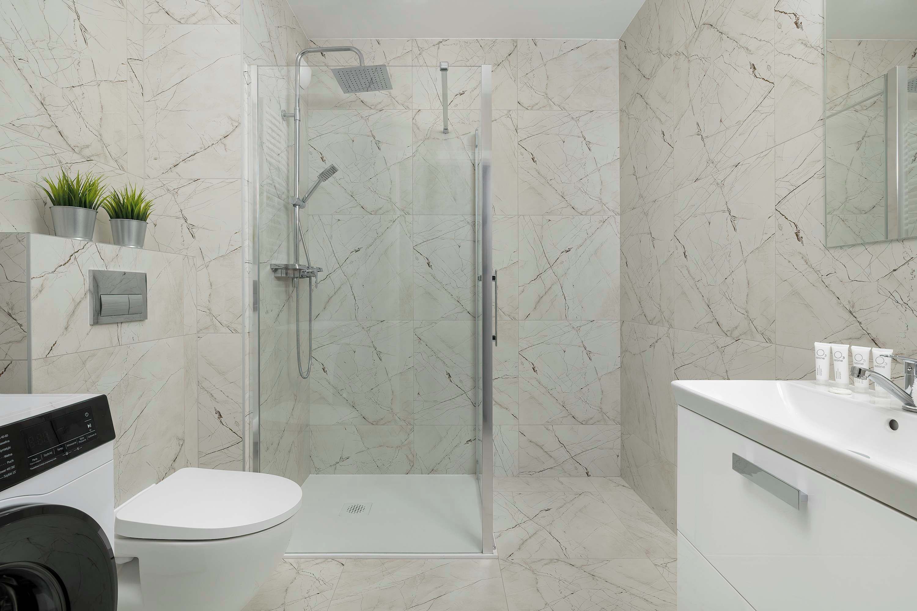 A modern bathroom with a glass-enclosed shower, a white toilet, and a sink with a mirror.