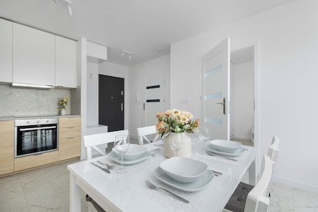 A modern kitchen with white cabinets, a built-in oven, and a dining area with a white table set for four.. Cozy Apartment with a Balcony | Parking