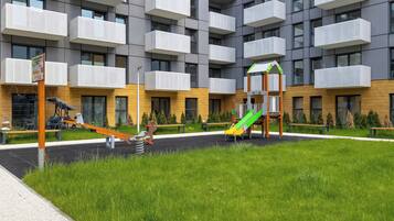 Un parque infantil con columpios, un tobogán, bancos y un edificio con balcones al fondo.