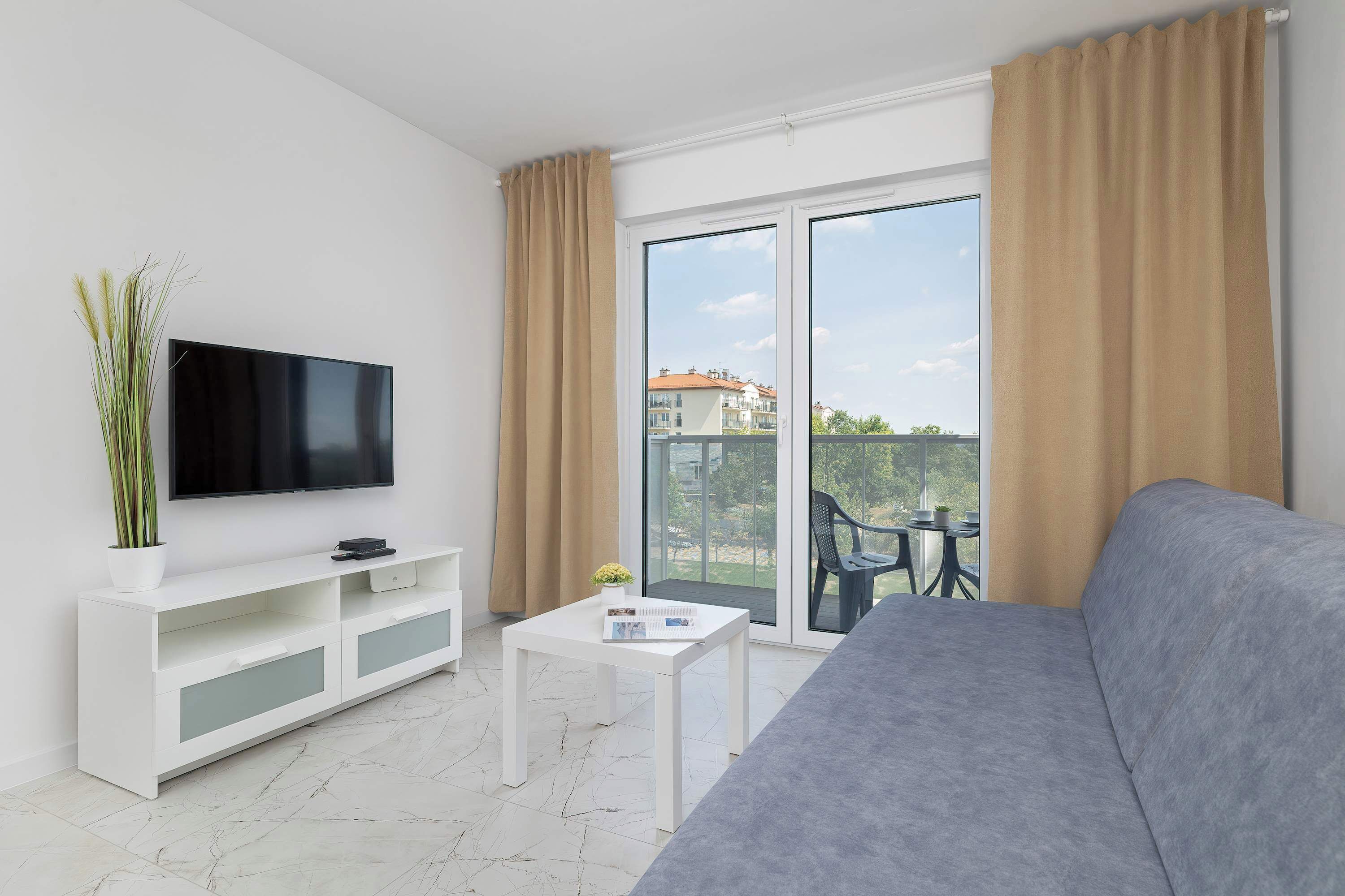 A modern living room with a flat-screen TV, a white console table, a grey sofa, and a sliding glass door leading to an outdoor area.