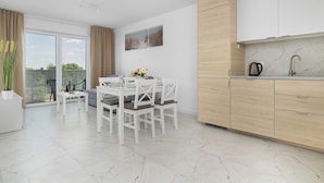 Een moderne keuken met witte kastjes, een eethoek met een witte tafel en stoelen, en uitzicht door de glazen deur.