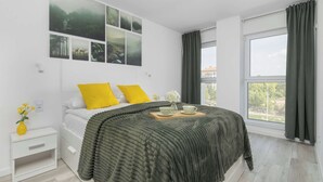 Een slaapkamer met een bed, nachtkastje, raam met gordijnen en wanddecoratie.