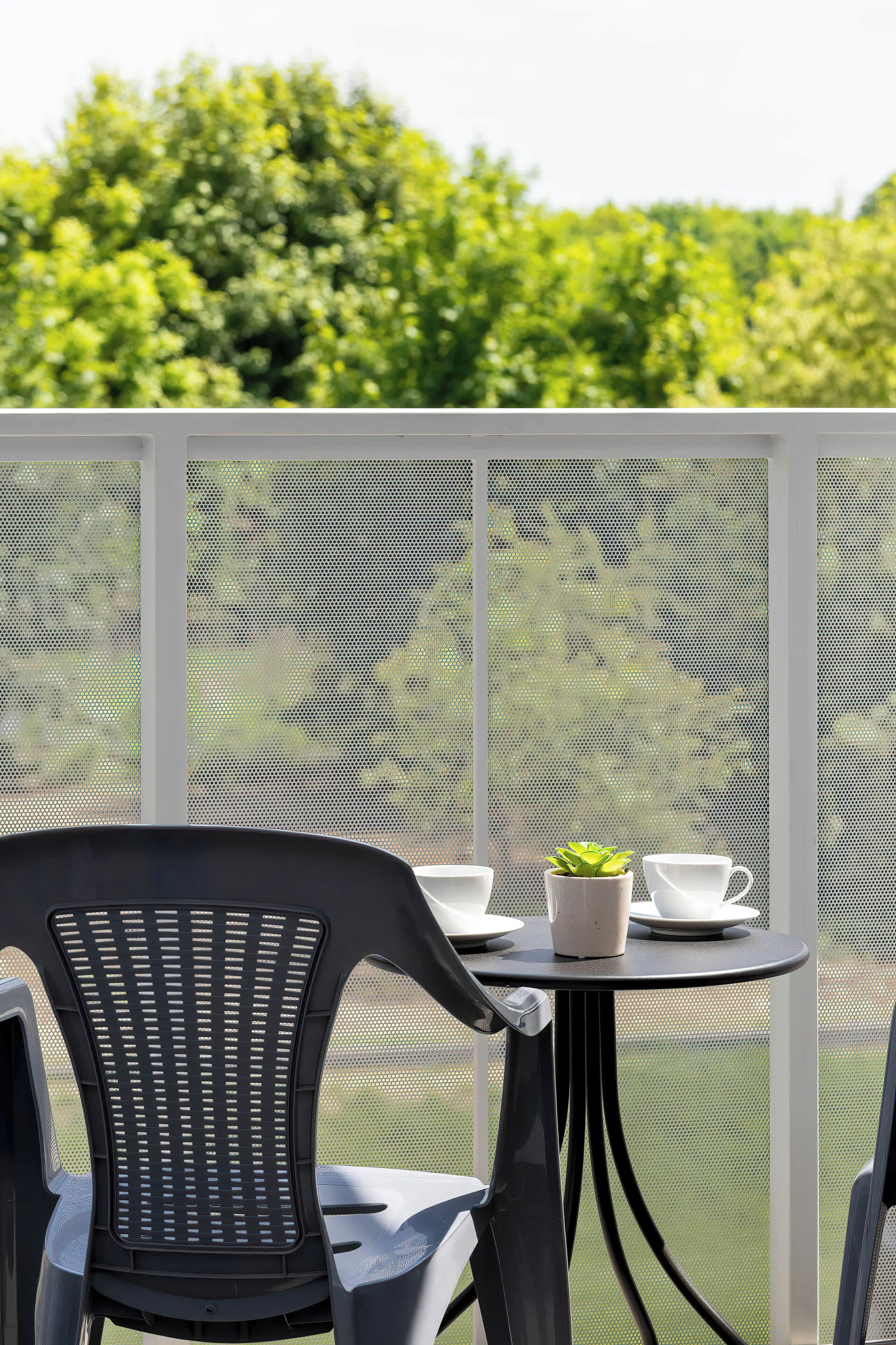 A balcony with a table, chairs, and a potted plant.