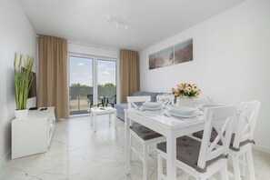 A modern dining area with a white table, chairs, and a glass-top table. There is a balcony with a view of the outdoors.