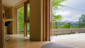 Ein geräumiges Zimmer mit großen Fenstern, einer Holzdiele und Blick auf Grünflächen und Berge.