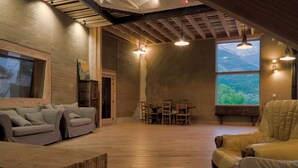 Ein geräumiger Loft mit hoher Decke, Holzbalken, einem großen Fenster mit Bergblick, einem Essbereich und einer Sitzecke mit Sofa und Sesseln.
