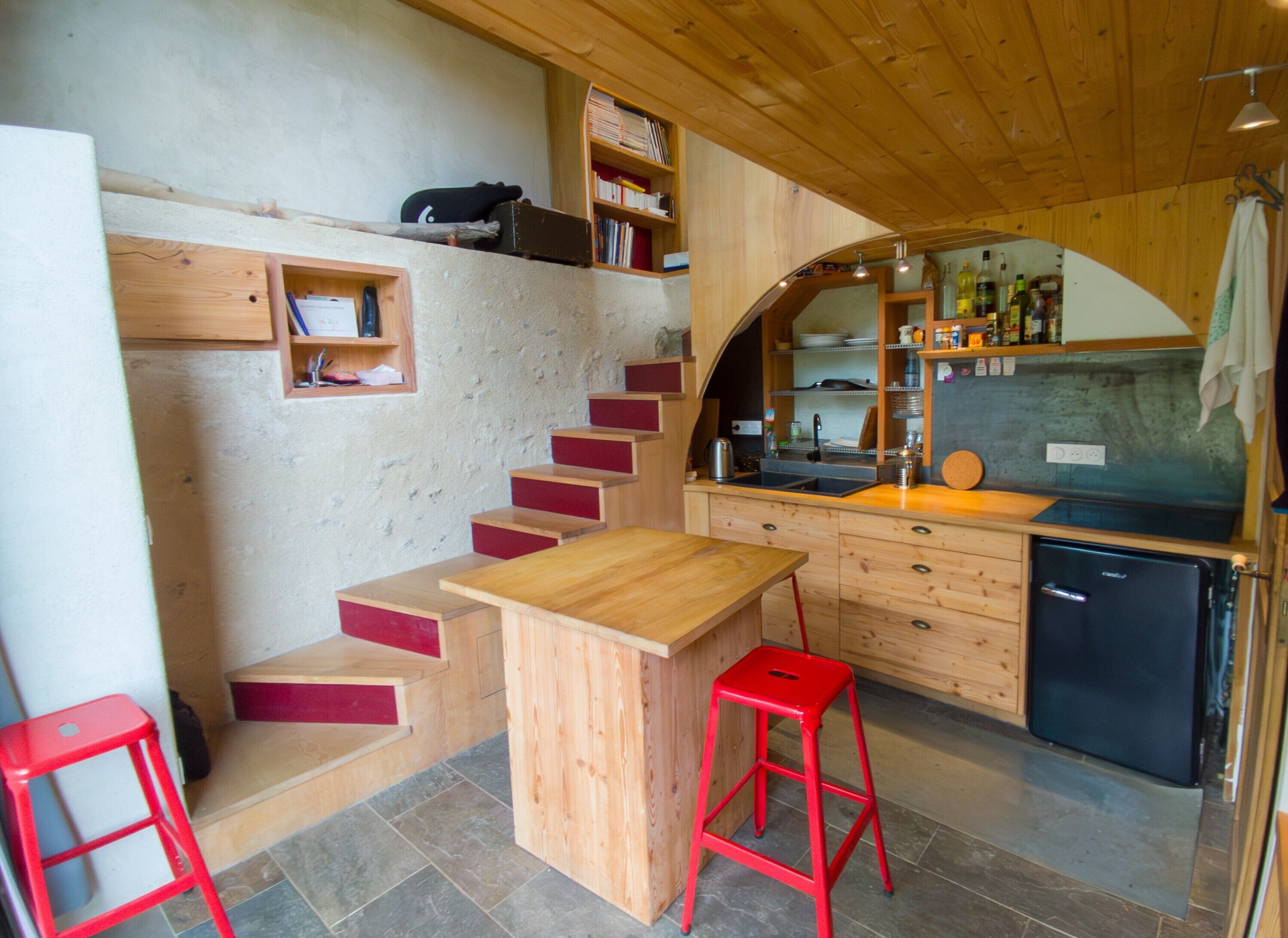 Eine kleine Küche mit Holztischplatte, einem Spülbecken, einem kleinen Kühlschrank und einem roten Hocker.