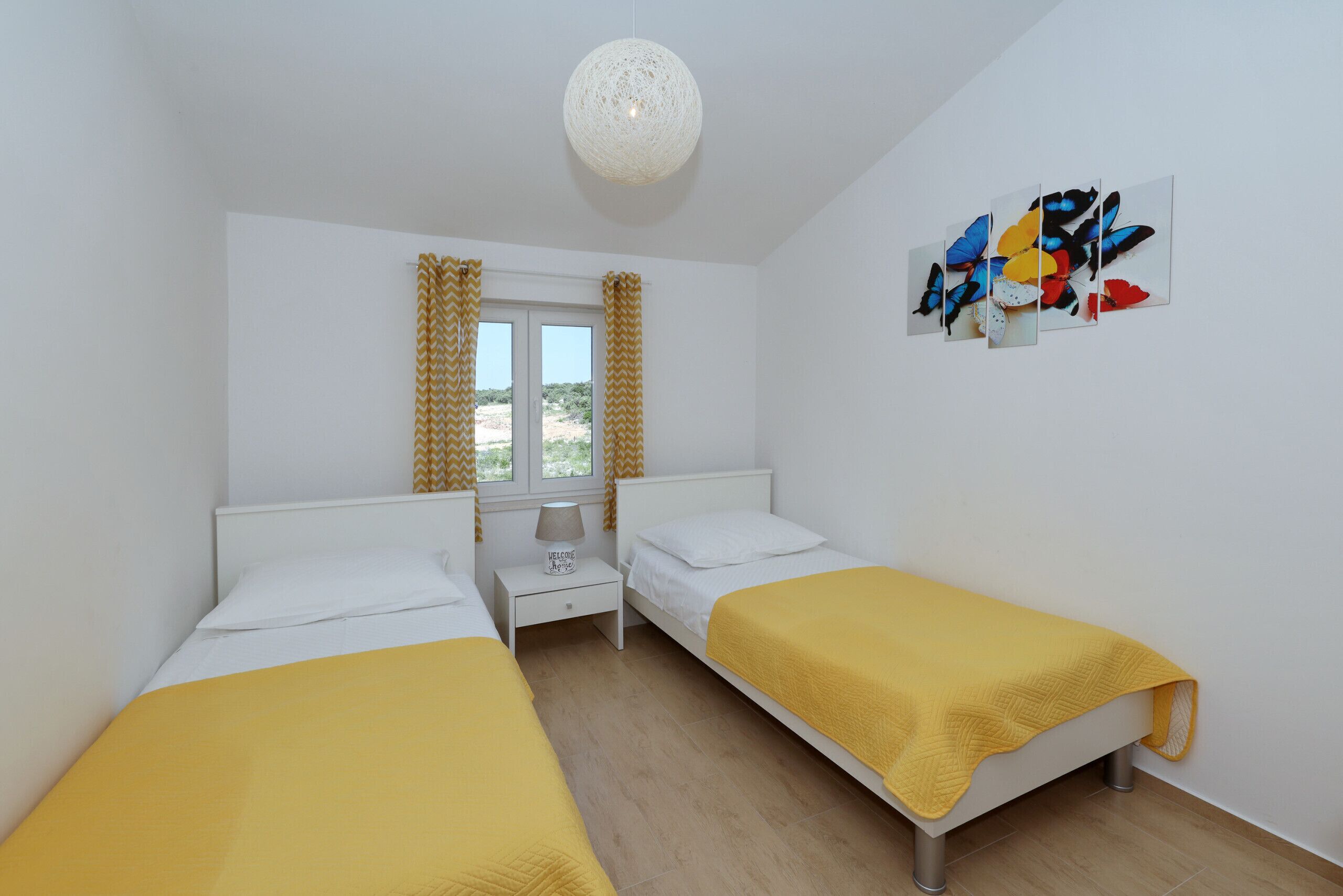 Ein Zimmer mit zwei Betten, einem fensterbelaubten Fenster, einem Wandbild und einer Deckenleuchte.