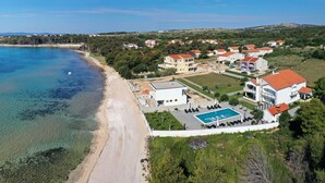 Luftaufnahme einer Küstenlandschaft mit Strand, Schwimmbad und Wohnhäusern.