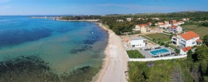 Luftaufnahme einer Küstenlandschaft mit Strand, Schwimmbad und Wohnhäusern.