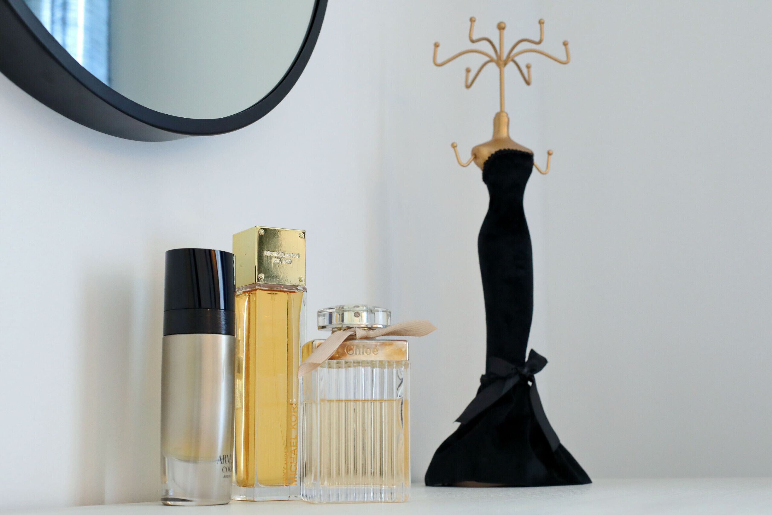 A mirror, a perfume bottle, a lighter, and a black dress on a white surface.
