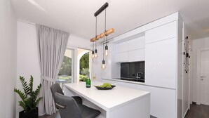A modern kitchen with white cabinetry, a central island, bar stools, a wine bottle, and a bowl of grapes. - Apartment Suva Punta 1 by the Sea (Vir)