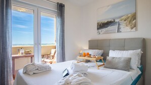 Una camera d'albergo con un letto, un vassoio per la colazione, un quadro e vista sulla spiaggia.