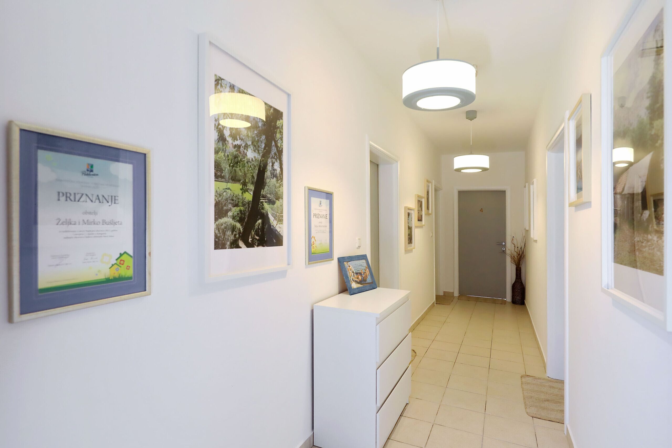 A hallway with framed certificates on the walls, a white cabinet, and a door at the end.