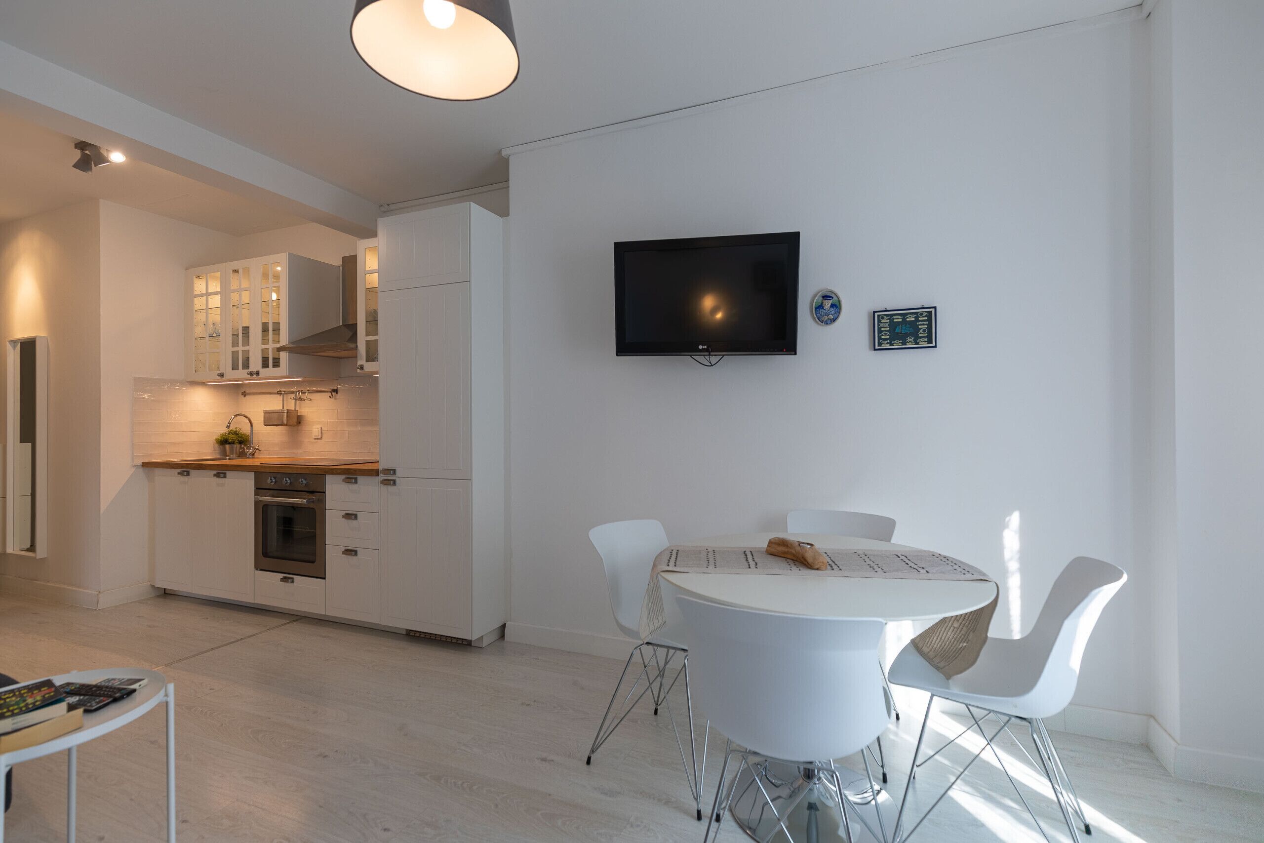A modern kitchen with white cabinets, a built-in oven, and a dining area with a round table and chairs.