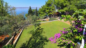 Ein Garten mit Rasen, Bäumen und Blick aufs Meer.