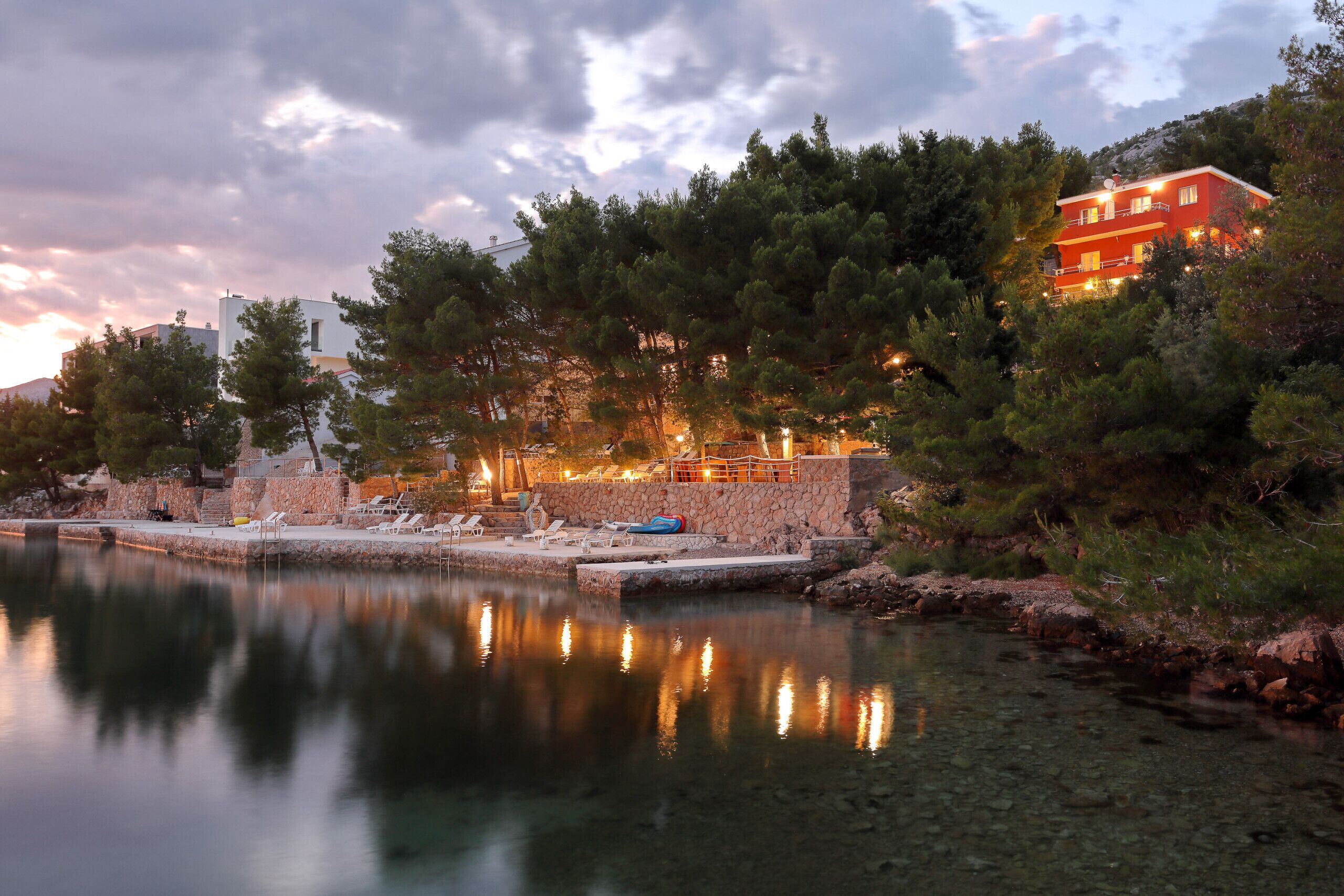 Une propriété située au bord de l’eau, avec un mur en pierre, un bâtiment rouge et un reflet net dans l’eau.