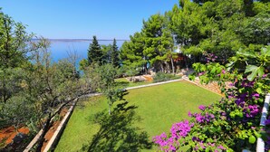 Un jardín con césped, árboles y vista al mar.