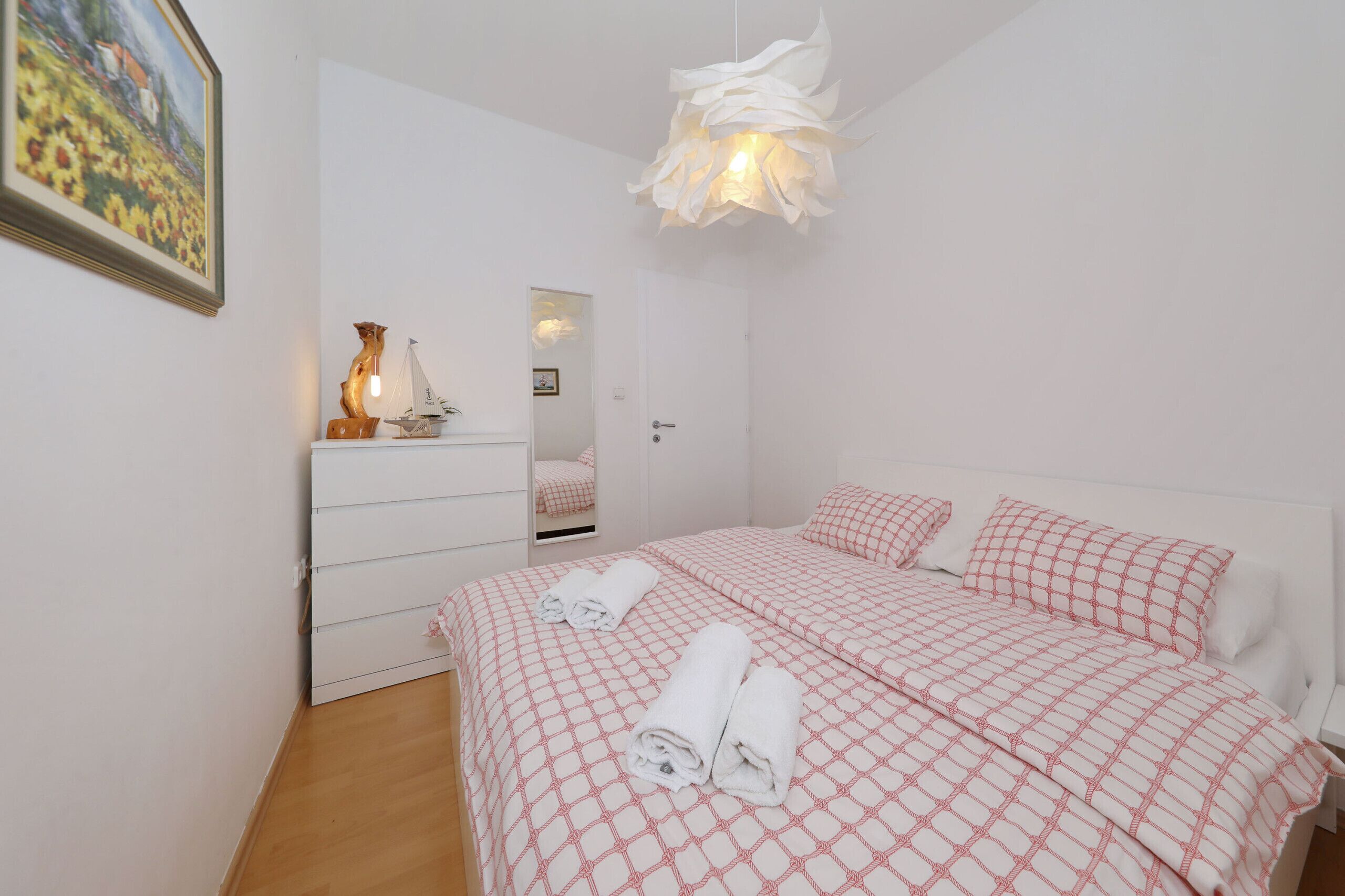 Une chambre à coucher comprenant un lit, une commode, un miroir et un luminaire suspendu.