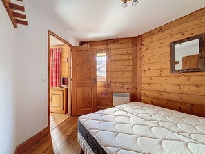 Ein Schlafzimmer mit Holzboden, einem Bett, einem Fenster und einer Tür zu einem anderen Raum.