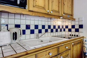 Una cocina con armarios de madera, un lavamanos blanco, una cafetera y un salpicadero de azulejos.