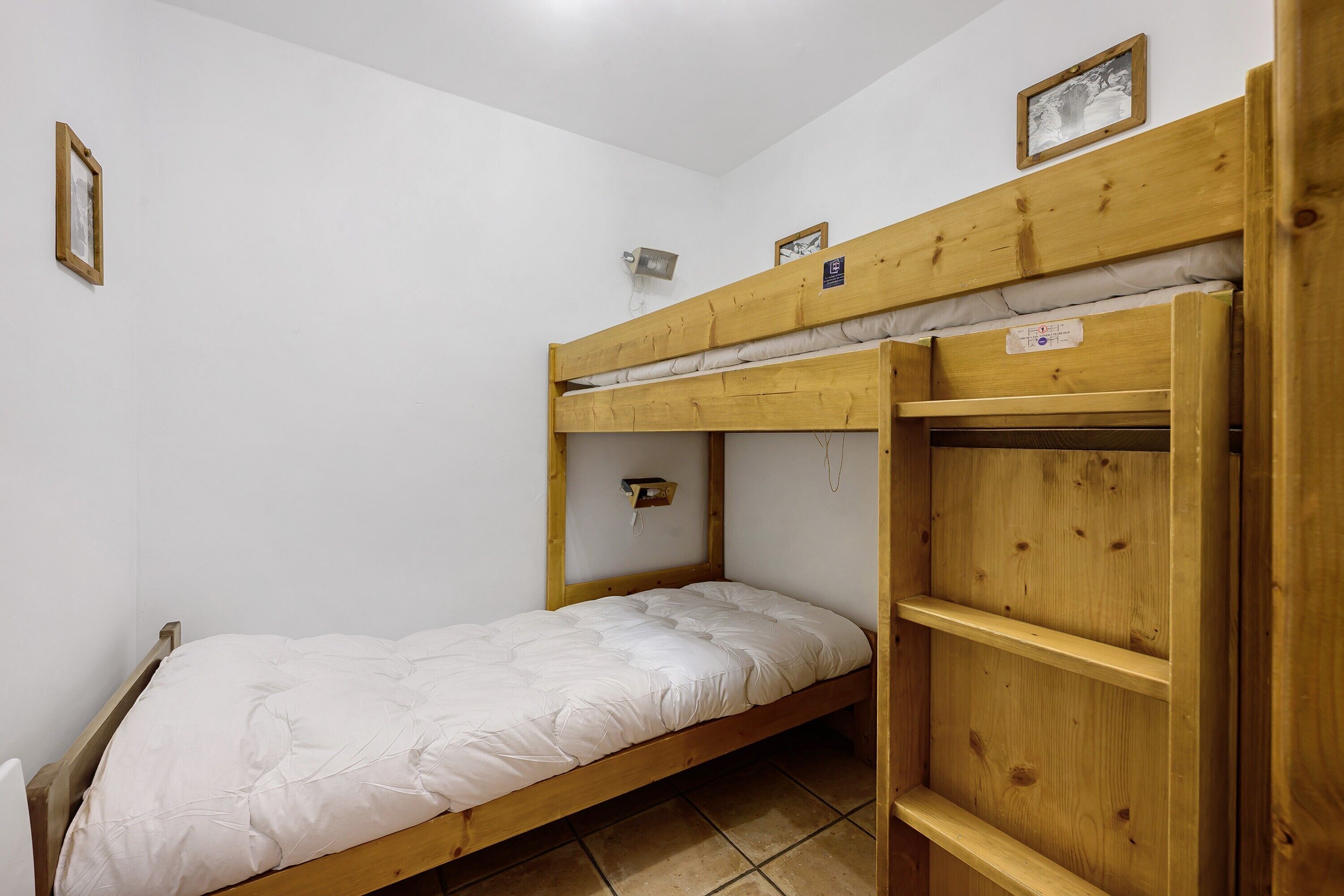 Une chambre avec un lit superposé, un matelas blanc, une tête de lit en bois et une petite étagère sur laquelle est posé un cadre photo.
