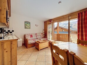 A cozy room with a wooden table, a sofa, and a kitchen area with a kettle and pots. - Apartment "Les Ancolies" with Balcony (Les Belleville)