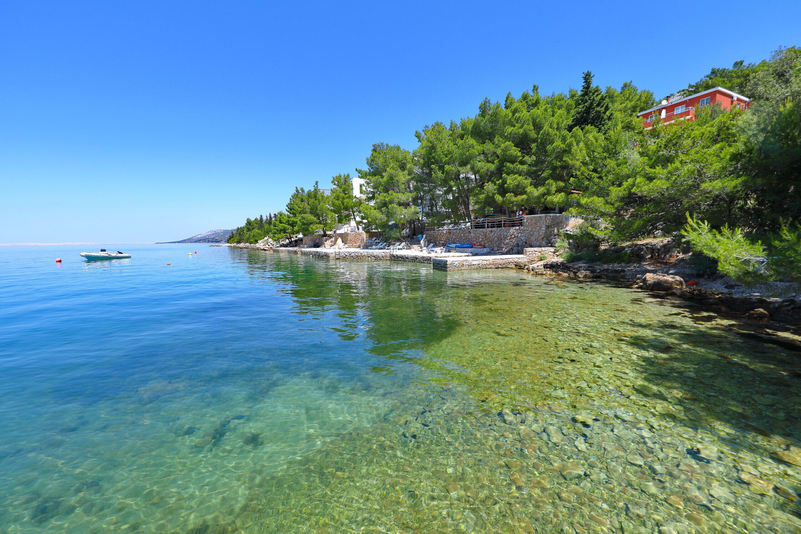 A clear coastal area with a stone pathway, a small boat, and a red building.