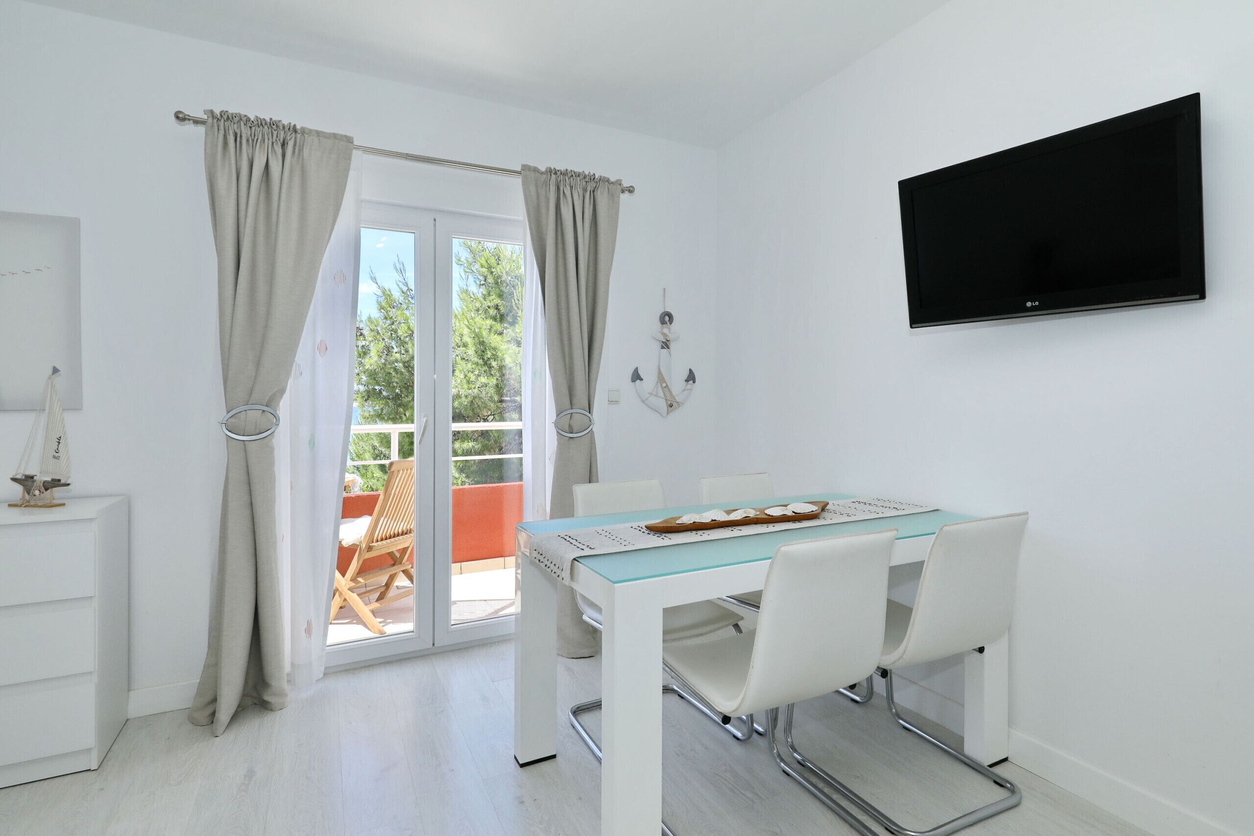 A modern room with a dining table, chairs, a flat-screen TV, and a sliding glass door leading to an outdoor area.