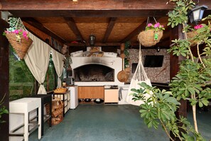 A rustic kitchen with a brick oven, wooden cabinets, and hanging baskets with flowers. - Apartment Anita with Outdoor Kitchen (Zadar)