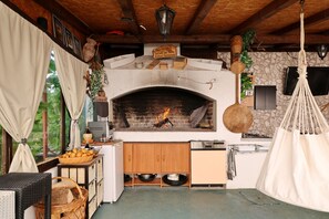 A rustic kitchen with a brick fireplace, wooden cabinets, and a hanging light fixture. - Apartment Anita with Outdoor Kitchen (Zadar)