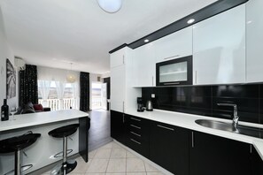 A modern kitchen with black and white cabinetry, a stainless steel sink, and a bar area with stools. - Apartment Marina No.2 with Sea View (Rovanjska)
