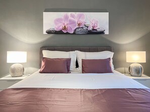 A neatly made bed with white and brown bedding, two bedside lamps, and a wall-mounted orchid artwork. - Apartment Marina No.2 with Sea View (Rovanjska)