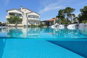 A swimming pool with lounge chairs, a large house with a balcony, and trees in the background. - Apartment Suva Punta 4 by the Sea (Vir)