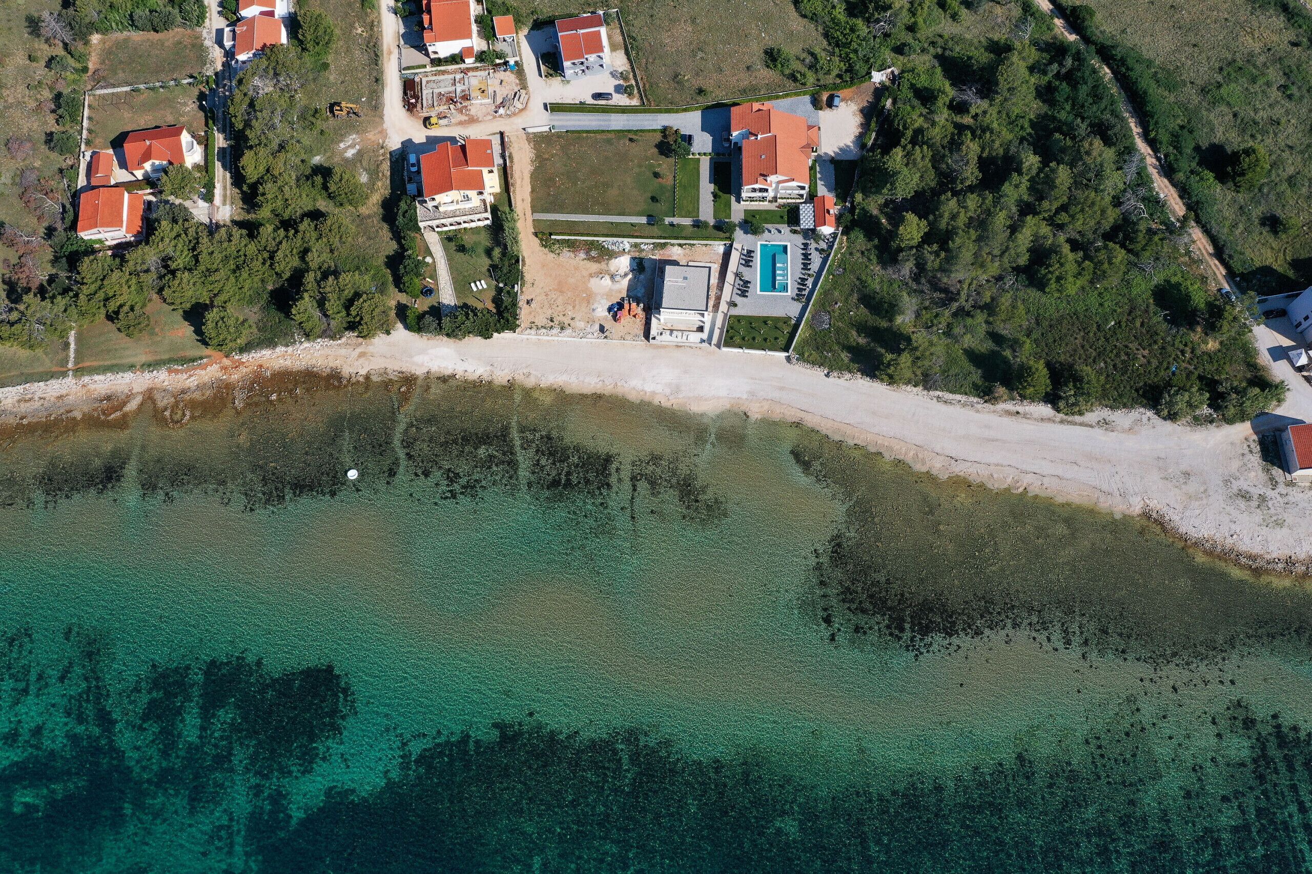 An aerial view of a coastal area with houses, a swimming pool, and a beach.