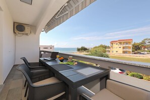 Ein Balkon im Freien mit Tisch, Stühlen und Blick auf das Meer und die Gebäude.
