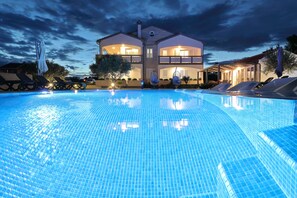 Une piscine avec des chaises longues et des parasols, un bâtiment à deux étages doté de balcons, et un ciel dégagé.