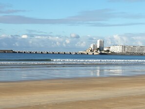 Ein Strand mit einem Steg, einer Reihe von Gebäuden und blauem Himmel.