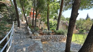 Un sentier de pierres qui monte une pente, bordé d’arbres et entouré d’un mur de pierres.
