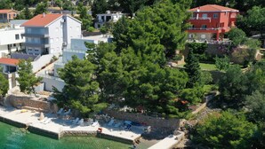 Vue aérienne d’une propriété située sur la côte, avec une plage, des chaises longues et un petit bateau.